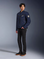 Veste Alpinestars Bruiser bleu foncé, veste de moto urbaine en textile au design inspiré du vêtement de travail, avec poches poitrine zippées et patch Oscar en spirale sur la manche, portée avec un pantalon noir et des baskets décontractées.