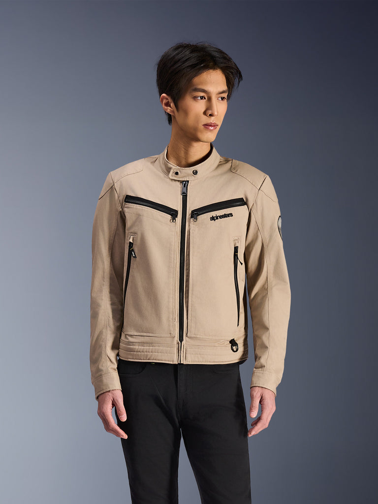 Alpinestars Bruiser Jacket, veste décontractée beige avec fermetures éclair noires, col montant, poches poitrine horizontales et poches latérales verticales, détails noirs contrastants, logo discret sur la poitrine