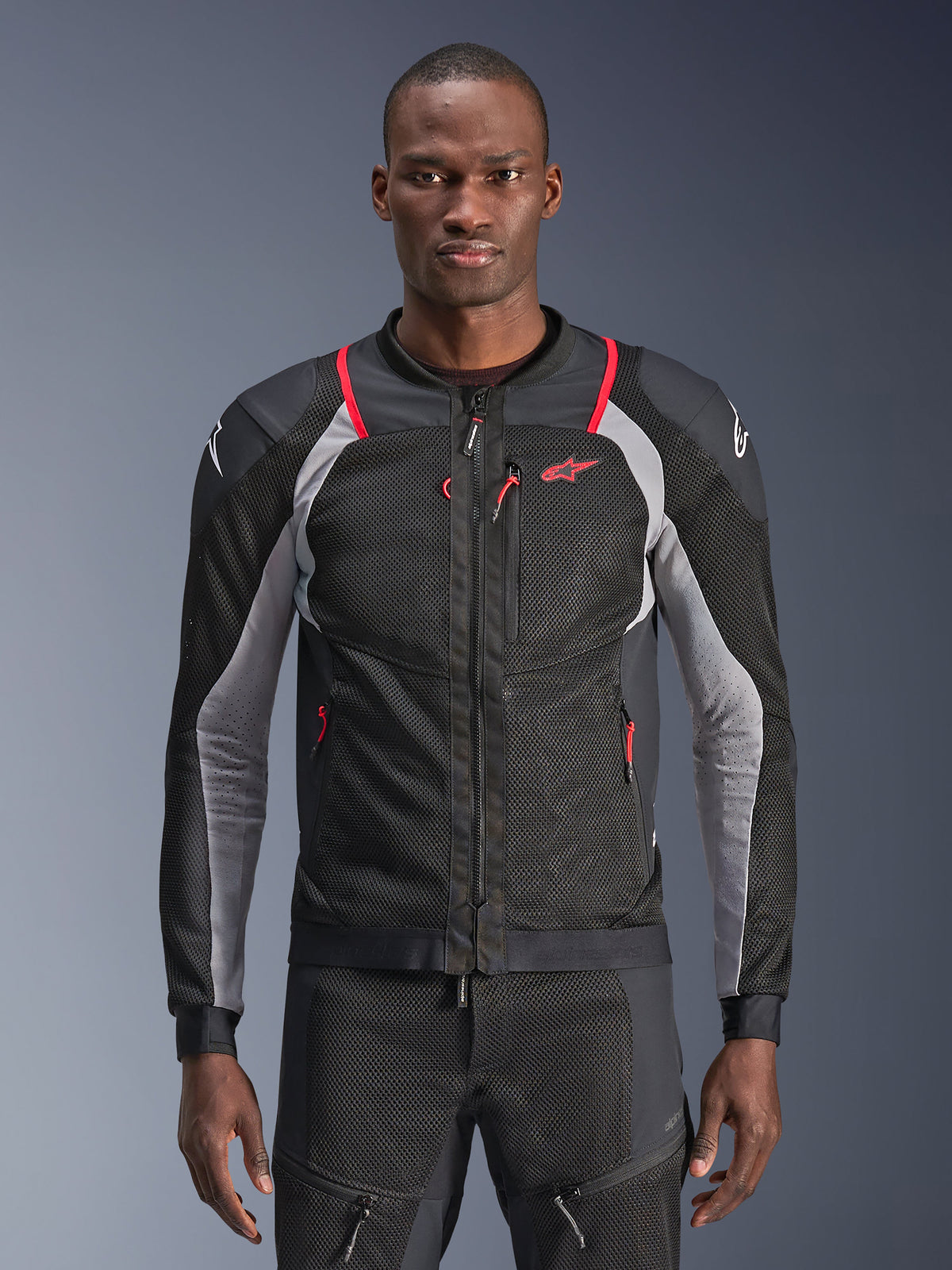 Veste Alpinestars Troop-Air Pro, veste d'air blindée technique premium, Noir Gris Cendre et Rouge Vif, construction en maille technique avec accents rouges sur les épaules et tirettes de fermeture éclair, détails gris sur les manches, et logo Alpinestars sur la poitrine et les épaules, portée par un mannequin sur un fond gris.