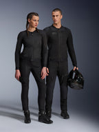 Alpinestars Stella Troop-Air Jacket, Man and woman wearing matching all-black technical motorcycle gear, featuring mesh construction for airflow, black pants and boots, man holding a black helmet, urban riding apparel.