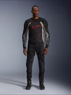 Männliches Model in der Alpinestars Troop-Air Jacke in Black Ash Gray und Bright Red, technische Mesh-Motorradjacke mit markantem roten Brustlogo, kombiniert mit schwarzer Motorradhose und Stiefeln, urbane Motorradbekleidung