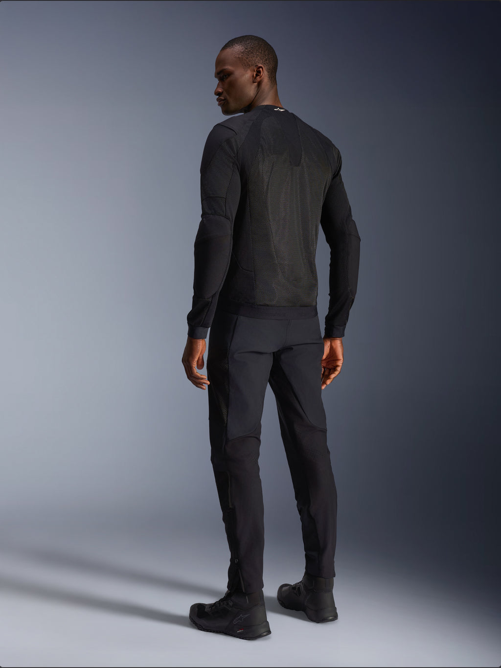Alpinestars Troop-Air Jacket, zwarte technische motorjas, achteraanzicht met grote mesh-panelen voor superieure ventilatie, gedragen met bijpassende zwarte broek en motorlaarzen, strak modern urban design voor zomerse ritten.