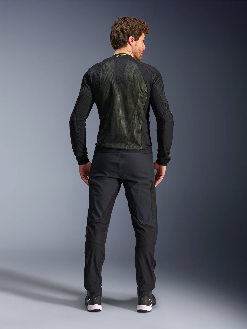 Alpinestars Troop-Air jas, Zwart Geel Fluo, achteraanzicht op een model, voorzien van een groot 2D tech mesh rugpaneel voor ventilatie, technische motorjas gedragen met zwarte motorbroek en laarzen, urban motorstijl