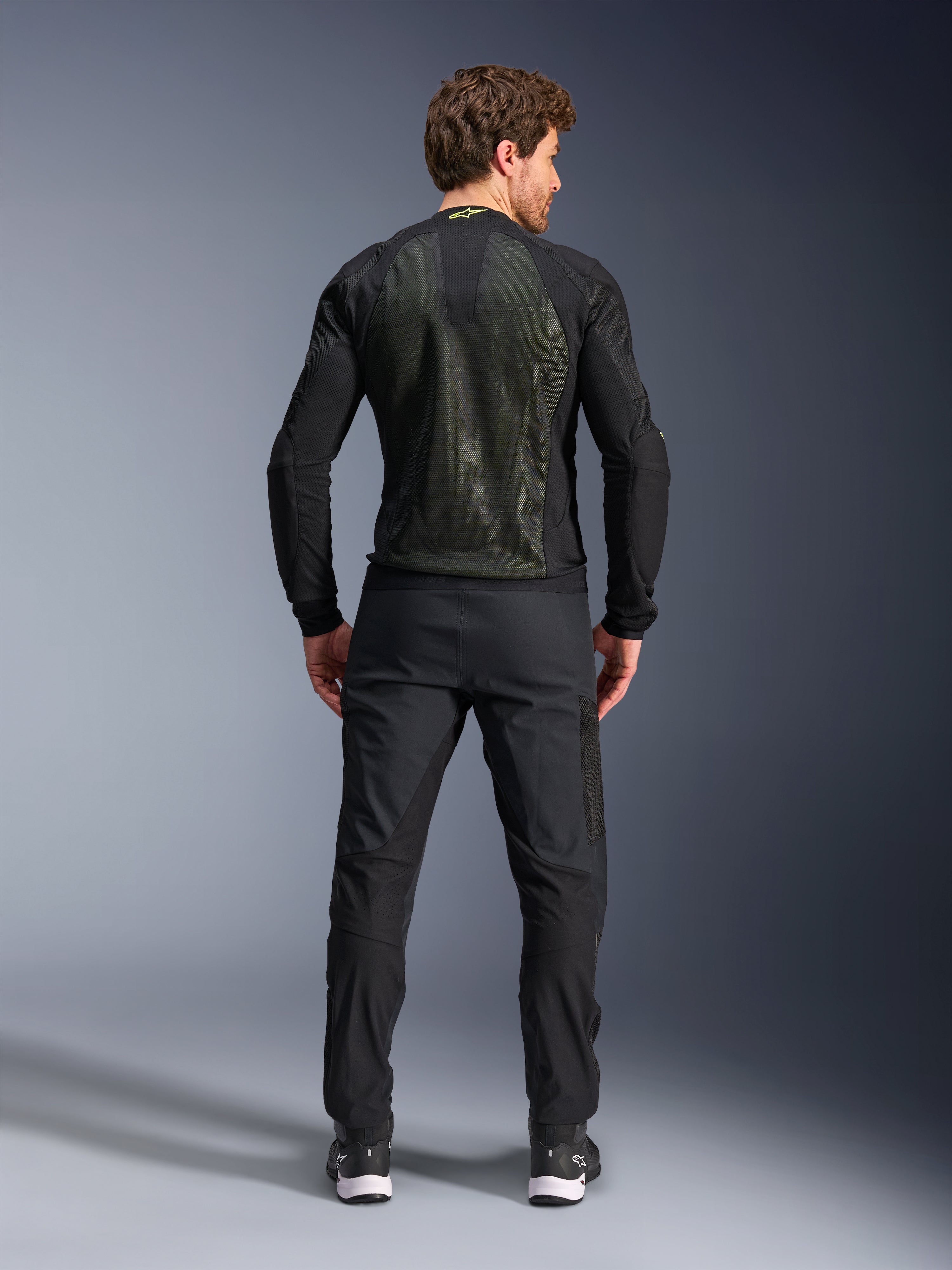 Alpinestars Troop-Air jas, Zwart Geel Fluo, achteraanzicht op een model, voorzien van een groot 2D tech mesh rugpaneel voor ventilatie, technische motorjas gedragen met zwarte motorbroek en laarzen, urban motorstijl