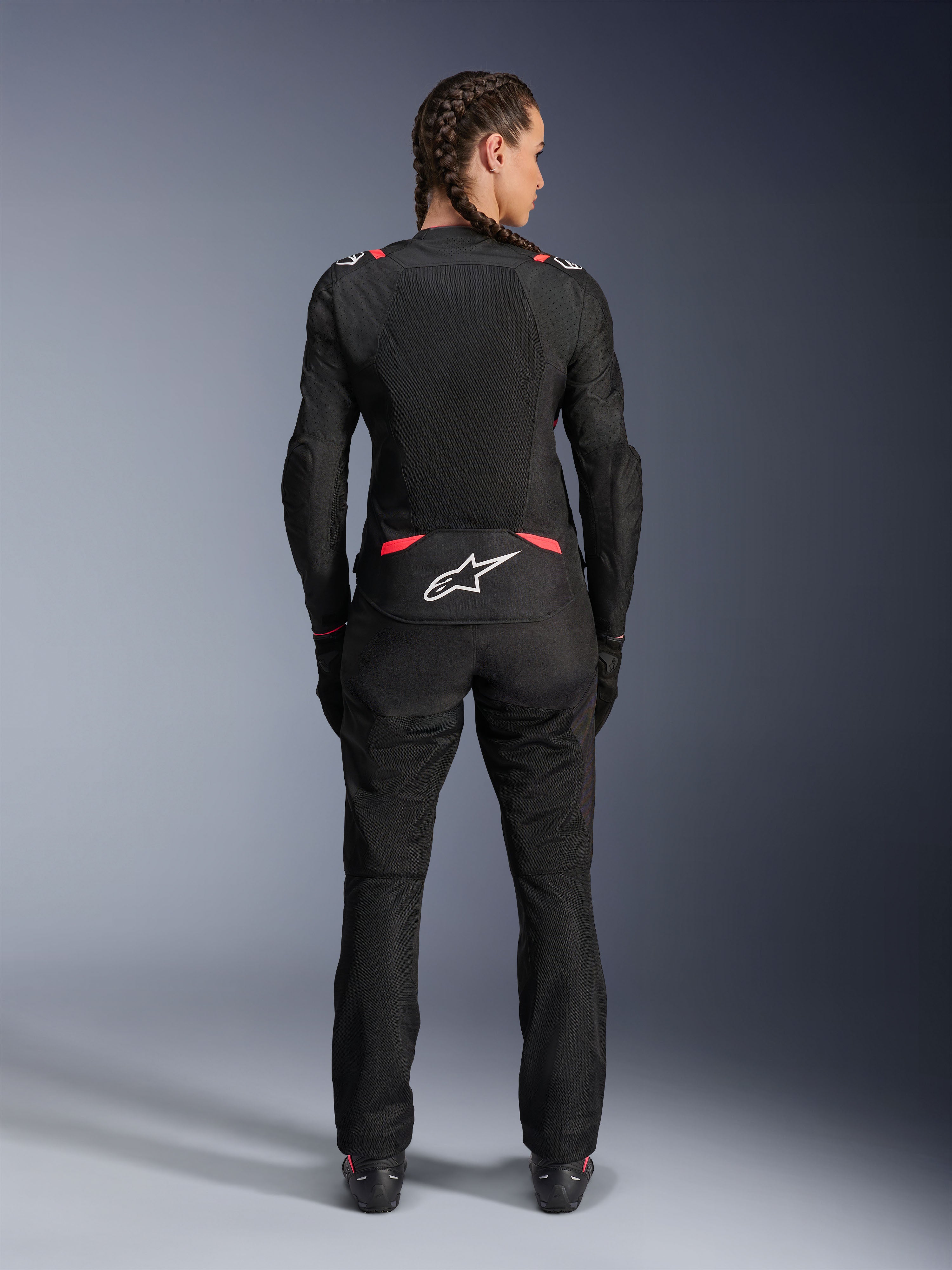 Alpinestars Stella T-SPS Air V2 Jacket, Women's Textile Motorcycle Jacket, Black and Diva Pink, rear view on model with braided hair, featuring large mesh panels for ventilation, white Astars logo on the lower back, paired with matching black riding pants.