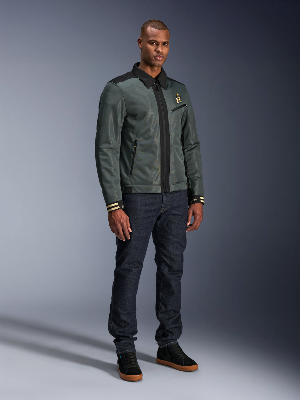 Veste Alpinestars Ignite Air, Urban Gray Black Blue, veste de moto urbaine, portée par un mannequin avec un jean en denim foncé et des baskets noires, dotée d'un corps en maille, d'un col de chemise traditionnel, d'une silhouette inspirée de la veste Harrington et d'un logo Alpinestars doré.