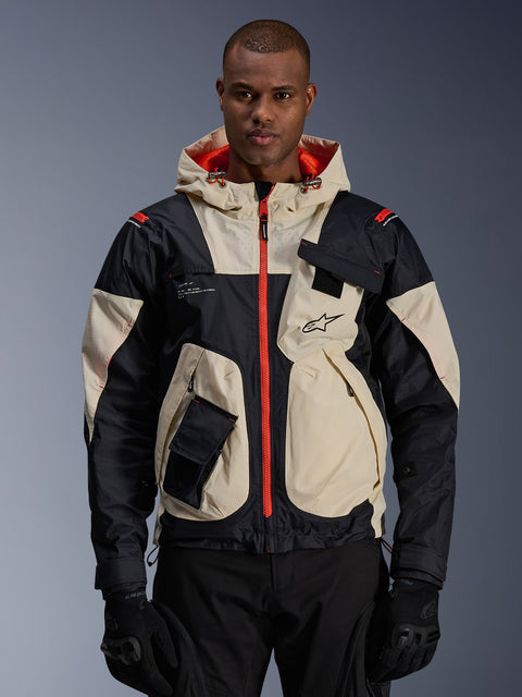 Alpinestars Mogress Air Jacket, veste de moto urbaine, amande et noir avec fermetures éclair et doublure de capuche orange vif, design à capuche avec poches utilitaires, logo sur la poitrine, portée avec des gants noirs