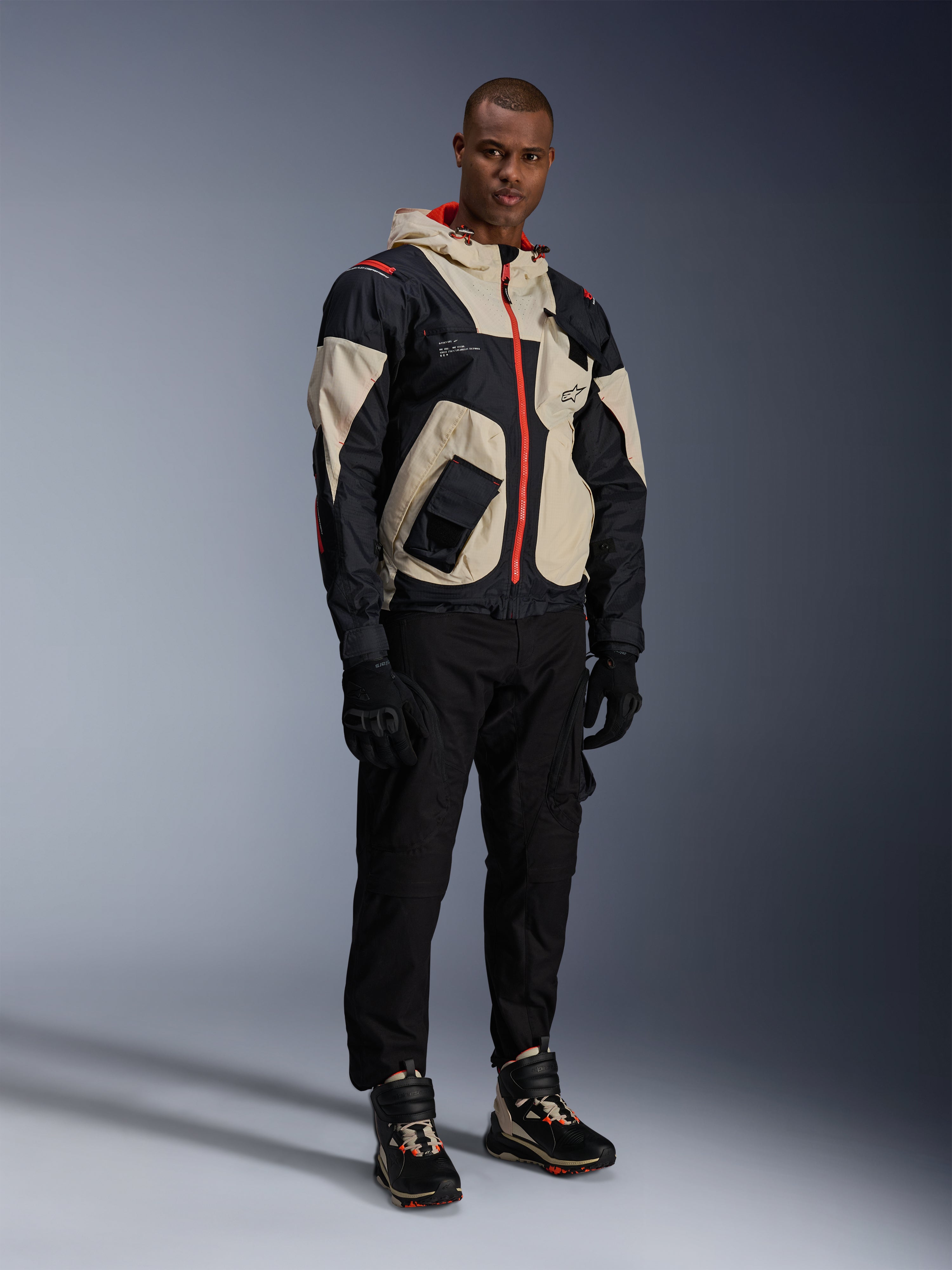 Man standing in full urban motorcycle gear, featuring Alpinestars Speedstreet Shoes in Black Almond Hot Orange and a Mogress Air Jacket in black and cream, coordinated black pants and gloves, streetwear-inspired protective outfit for street riding