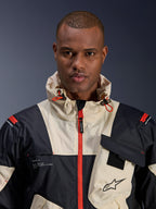 Male model wearing Alpinestars Mogress Air Jacket, Urban Motorcycle Jacket, Black Almond and Hot Orange, close-up view showing the color-blocked design, ripstop texture, hooded collar with orange toggles, and front zipper details.