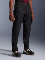 Alpinestars Acteon Pants, Black Motorcycle Pants, worn by a model, featuring a modern tapered silhouette, zippered cargo pockets, adjustable waist belt, and technical sneakers, urban riding apparel