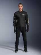 Modèle masculin portant la veste Alpinestars T-Dyno Air, noire, veste de moto légère en textile avec maille 3D respirante, logos d'étoiles blanches sur les manches, avec pantalon, gants et bottes noirs, vue de face debout