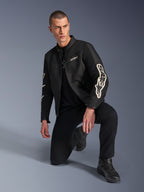 Modèle masculin portant la veste Alpinestars T-Dyno Air, veste de moto textile noire avec un large logo blanc sur les manches, associée à un pantalon noir et des bottes de moto, design moderne d'inspiration vintage avec panneaux en maille 3D.