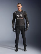 Veste Alpinestars T-Stunt Air, veste de moto noire et blanche, portée avec un pantalon de moto, des gants et des bottes noirs, logo Alpinestars blanc sur la poitrine et les manches, conception textile à coupe sportive avec panneaux en mesh pour la ventilation