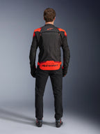 Alpinestars T-Stunt Air Jas, zwart met Red Fluo en Dark Red accenten, achteraanzicht op model, gecombineerd met zwarte motorbroek en laarzen, opvallende Alpinestars-branding op het onderste rugpaneel, modulair ontwerp met mesh-constructie voor ventilatie