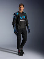 Männliches Model in Alpinestars T-Stunt Air Jacke, Schwarz, Dunkelblau und Blithe Blue, mit markanten Mesh-Einsätzen für Luftzirkulation, kombiniert mit schwarzer Hose und Motorradhandschuhen, sportlich geschnittene Motorradjacke für sommerliche Straßenfahrten