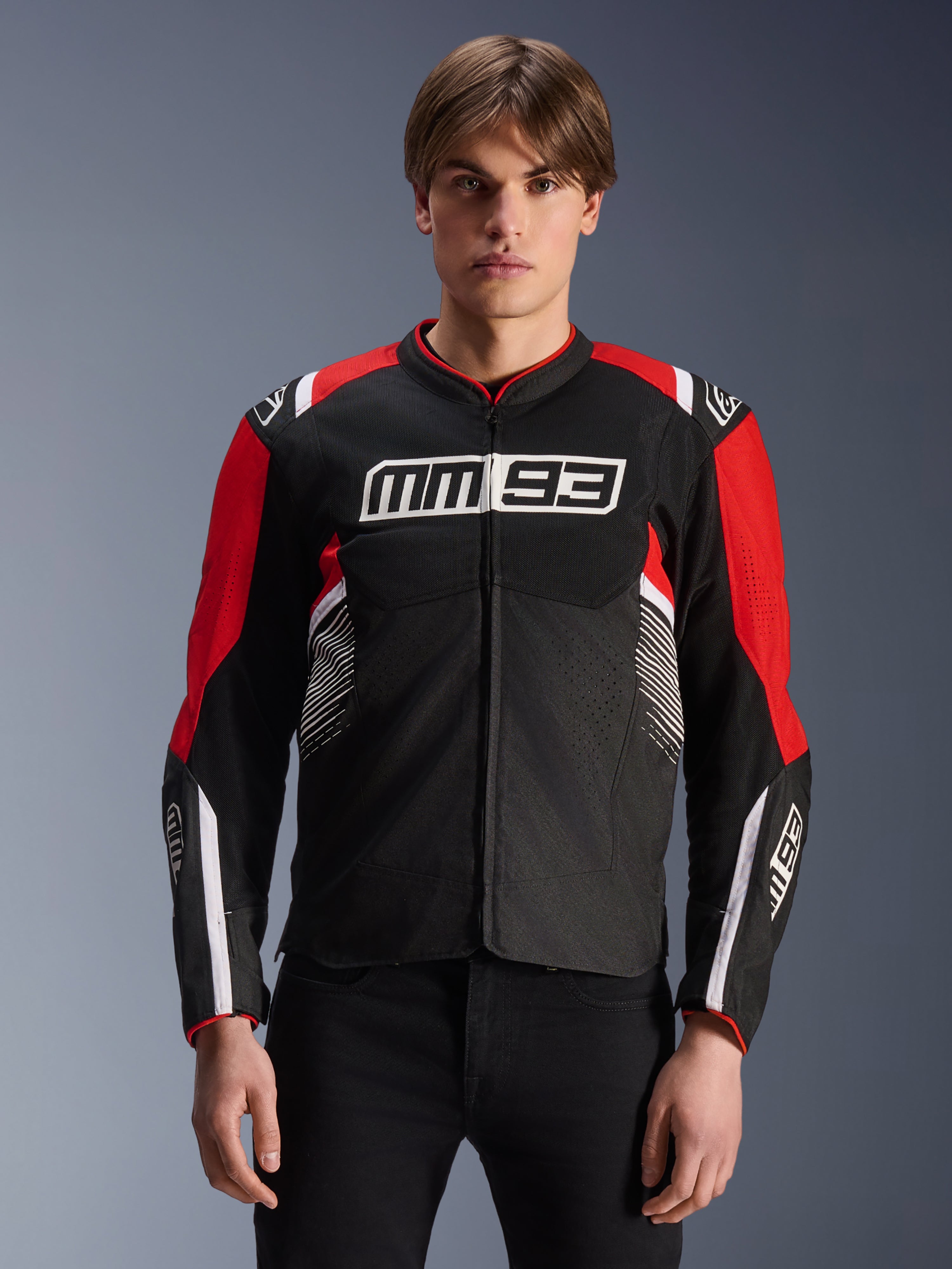 MM93 T-SPS Air V2 Jacke, Textil-Motorradjacke in Schwarz, Bright Red und Weiß, mit Marc Márquez MM93-Branding auf Brust und Ärmeln, Mesh-Einsätze zur Belüftung, sportliches Design, getragen von einem Model mit schwarzer Hose