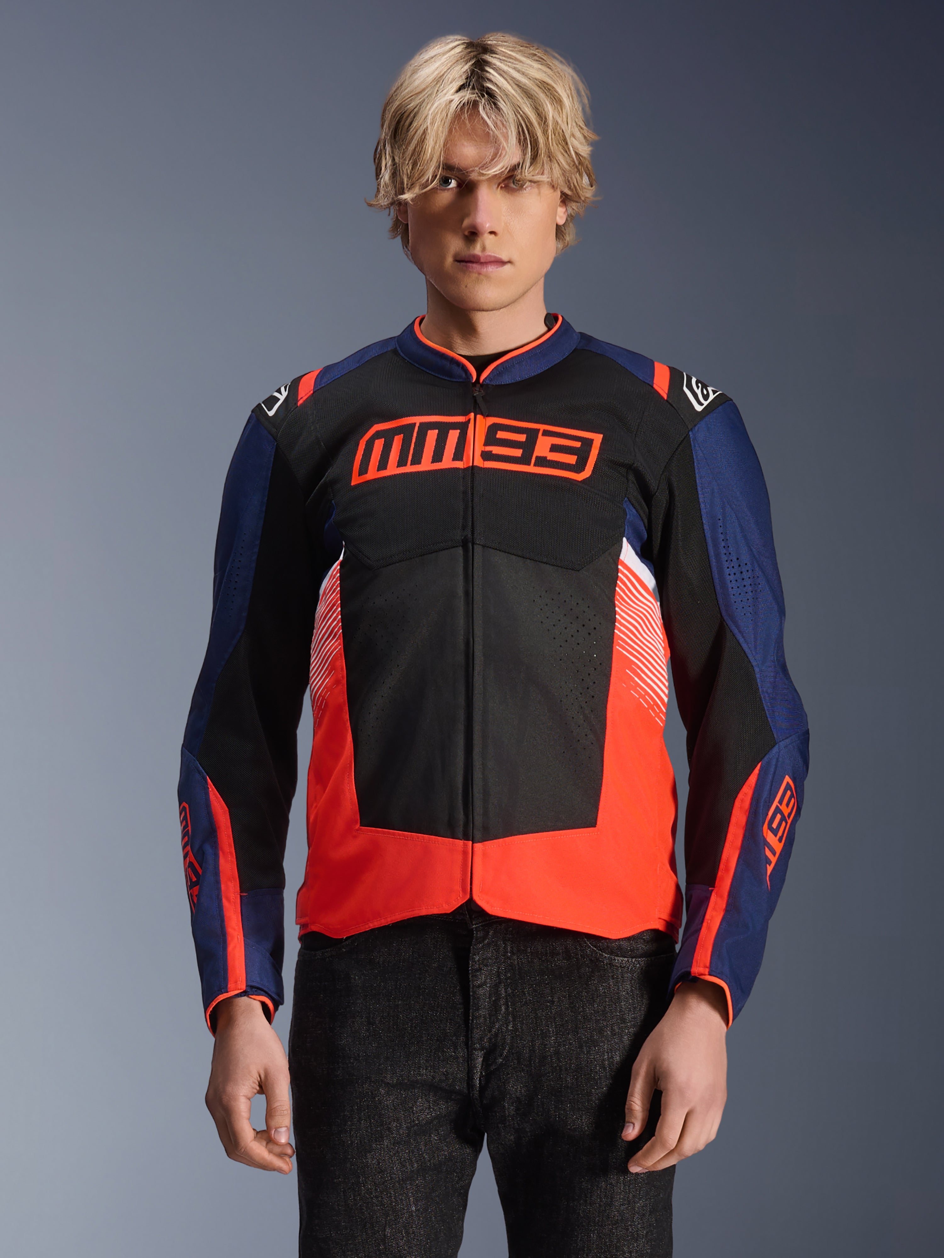 Alpinestars MM93 T-SPS Air V2 Jacke, Textil-Motorradjacke, Marineblau, Schwarz und Fluo-Rot, getragen von einer Person, mit markantem MM93-Branding auf der Brust, Mesh-Einsätzen zur Belüftung und modernem Color-Blocking-Design