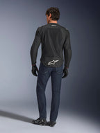 Alpinestars FQ20 T-SPS Air V2 Monster Jas, zwart, achteraanzicht op model met donkerblauwe jeans en zwarte motorlaarzen, voorzien van een groot wit logo op de onderrug en ademende mesh-panelen, stedelijke sportieve motoruitrusting.