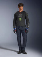 Mannelijke rijder die de Alpinestars FQ20 T-SPS Air V2 Monster jas draagt, zwart met groen Monster Energy-logo en witte '20' graphic op de borst, gecombineerd met een donkerblauwe jeans en technische motorhandschoenen, urban sportieve motoroutfit.
