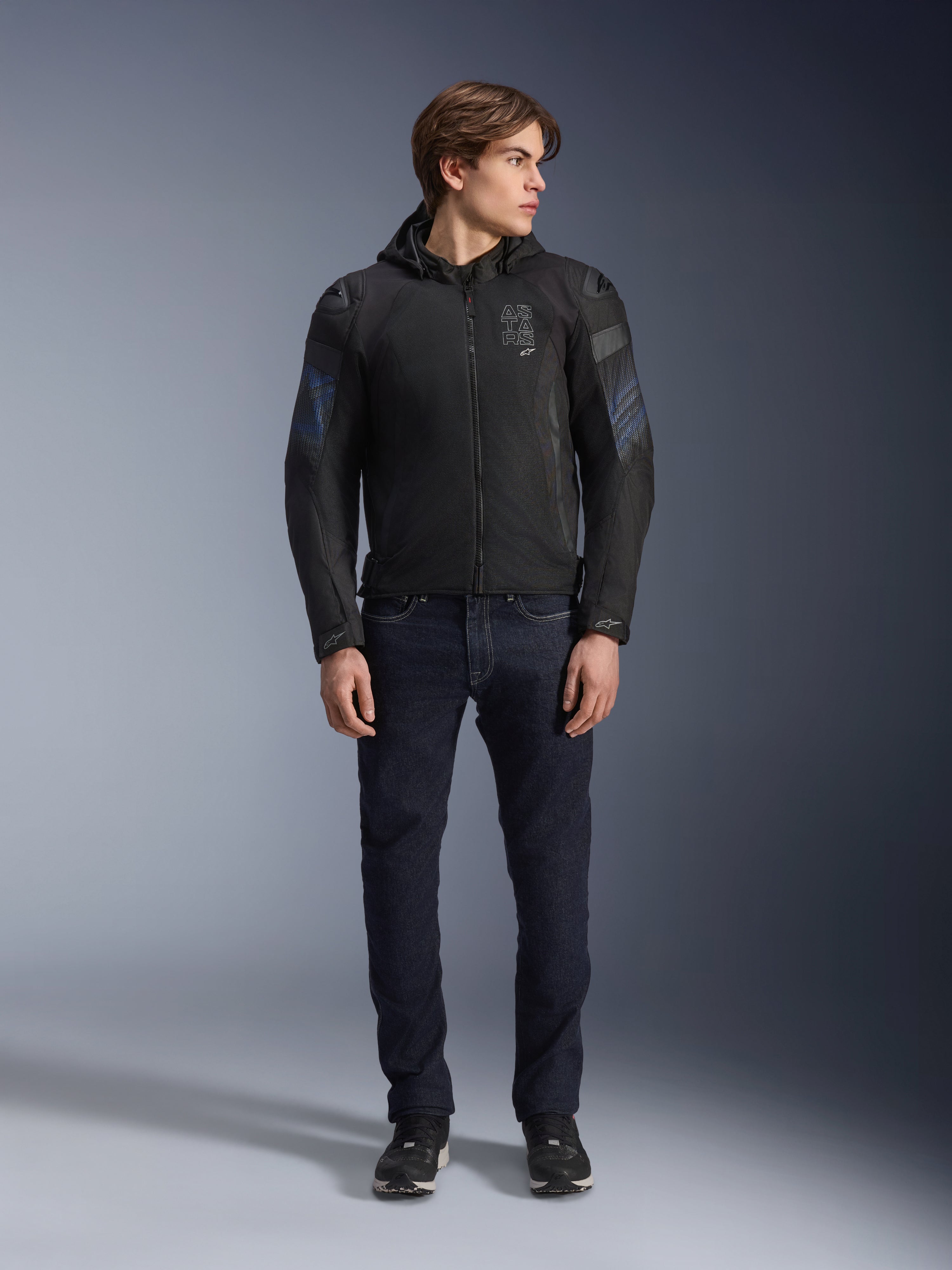 Männliches Model trägt die Alpinestars Zaca Air Venom WP Jacke in Schwarz und Electric Blue, Textil-Motorradjacke mit 3D-Mesh-Einsätzen und abnehmbarer Kapuze, kombiniert mit einer dunklen Denim-Jeans, moderne sportlich inspirierte Fahrausrüstung