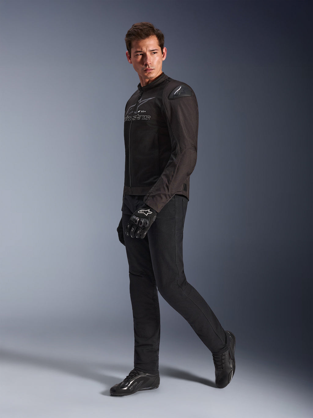 Veste Alpinestars SMX Air en Noir Anthracite, portée par un mannequin avec pantalon de moto, gants et chaussures noirs assortis, cliché studio en pied, équipement moto sport de performance avec maille technique et sliders d'épaule