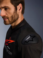 Veste Alpinestars SMX Air, noir et rouge, gros plan sur la protection d'épaule DFS Lite avec logo en étoile, portée par un homme barbu, veste de moto textile sport et racing.