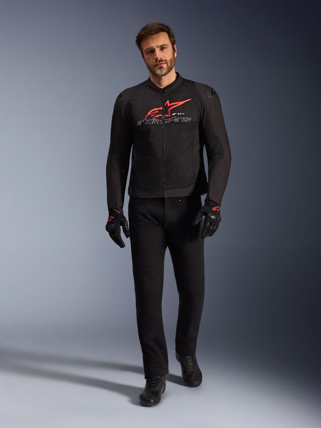 Veste Alpinestars SMX Air, noir, rouge vif et blanc, veste de moto sportive portée avec un pantalon et des gants de moto noirs, dotée de panneaux en maille technique et d'un logo Alpinestars rouge vif sur la poitrine, tenue de route haute performance