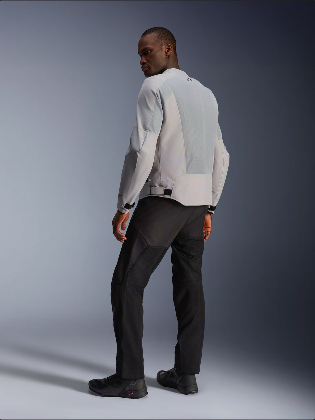 Alpinestars C-1 Air Jacket, Silver and Gray, viewed from the back on a model, featuring ventilated tech mesh panels and reflective logos, worn with black pants and shoes, urban contemporary motorcycle riding gear.