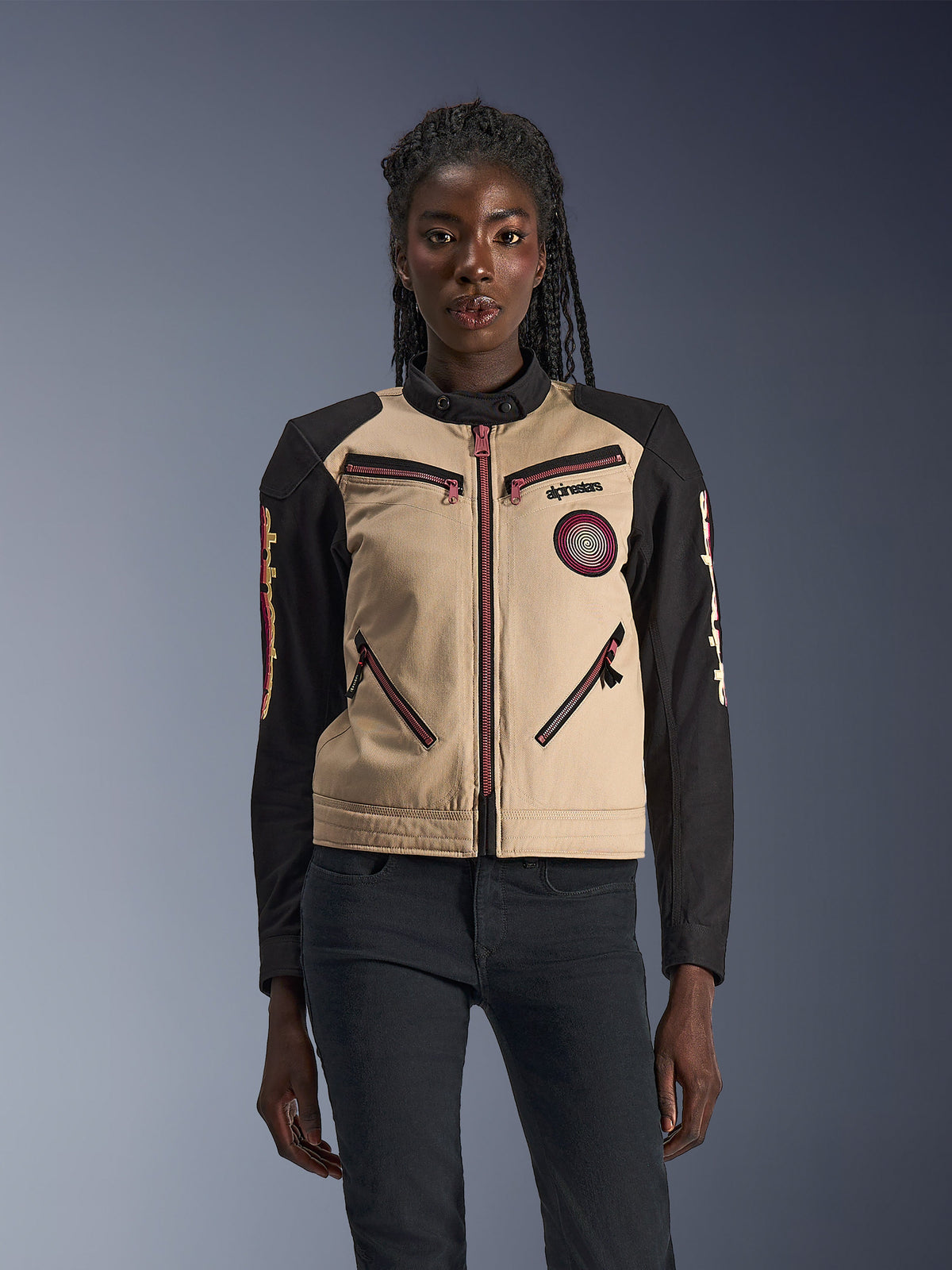 Veste Alpinestars Stella Grace, veste de moto pour femme, aluminium et noir, design d'inspiration workwear avec fermetures éclair rouge rosé, écusson en spirale sur la poitrine et manches noires avec motifs jaunes et rouges, portée par un mannequin