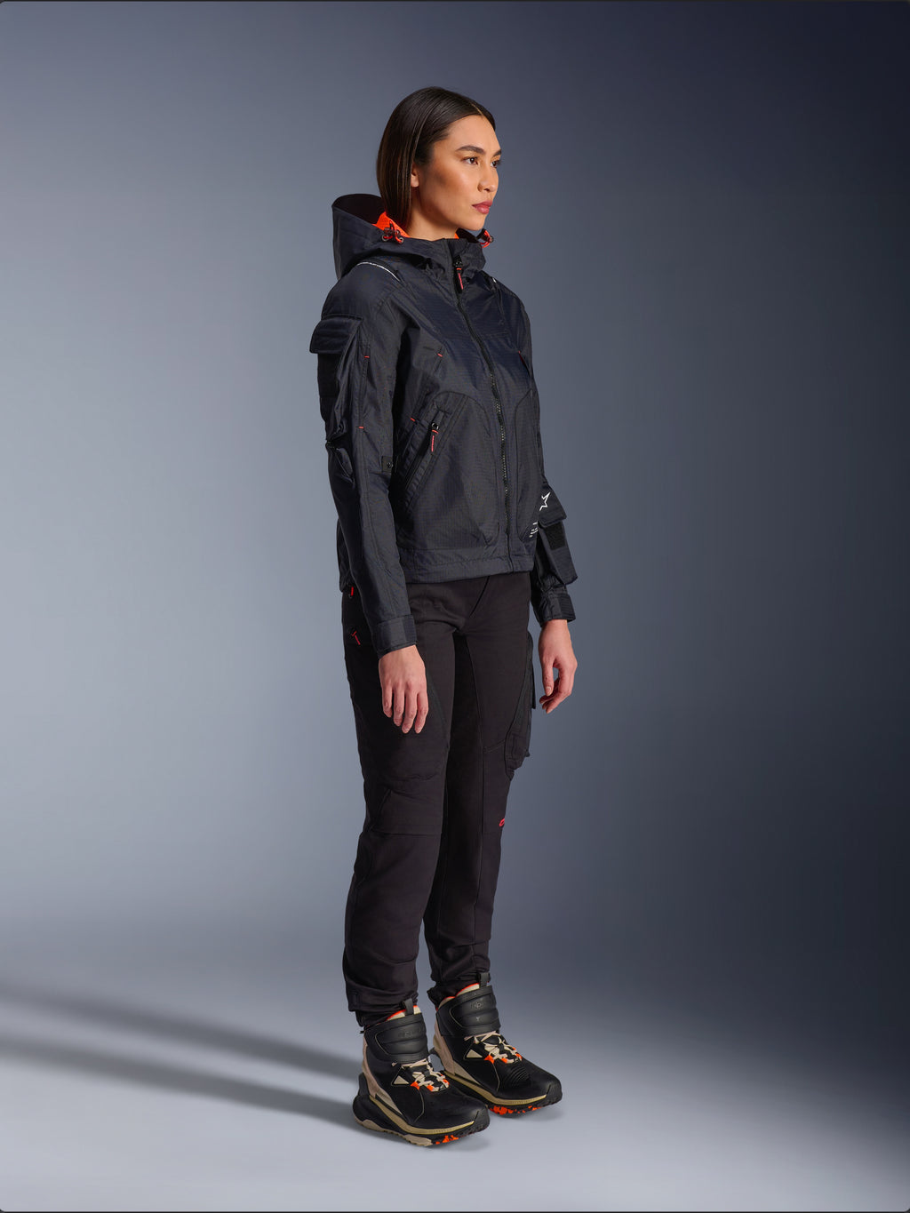 Alpinestars Actea damesbroek in het zwart, regular fit met cargozakken, gecombineerd met een zwart Molly Air Jacket met oranje accenten en hoge motorschoenen, eigentijdse urban motorkleding voor dames