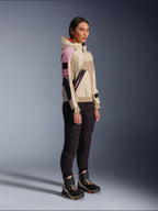 Vrouwelijk model draagt de Alpinestars Molly Air Jacket in Sand Pink Almond, gecombineerd met een donkere technische broek en hoge motorschoenen, urban motorjas voorzien van een capuchon en meerkleurige panelen, eigentijds op streetwear geïnspireerd ontwerp