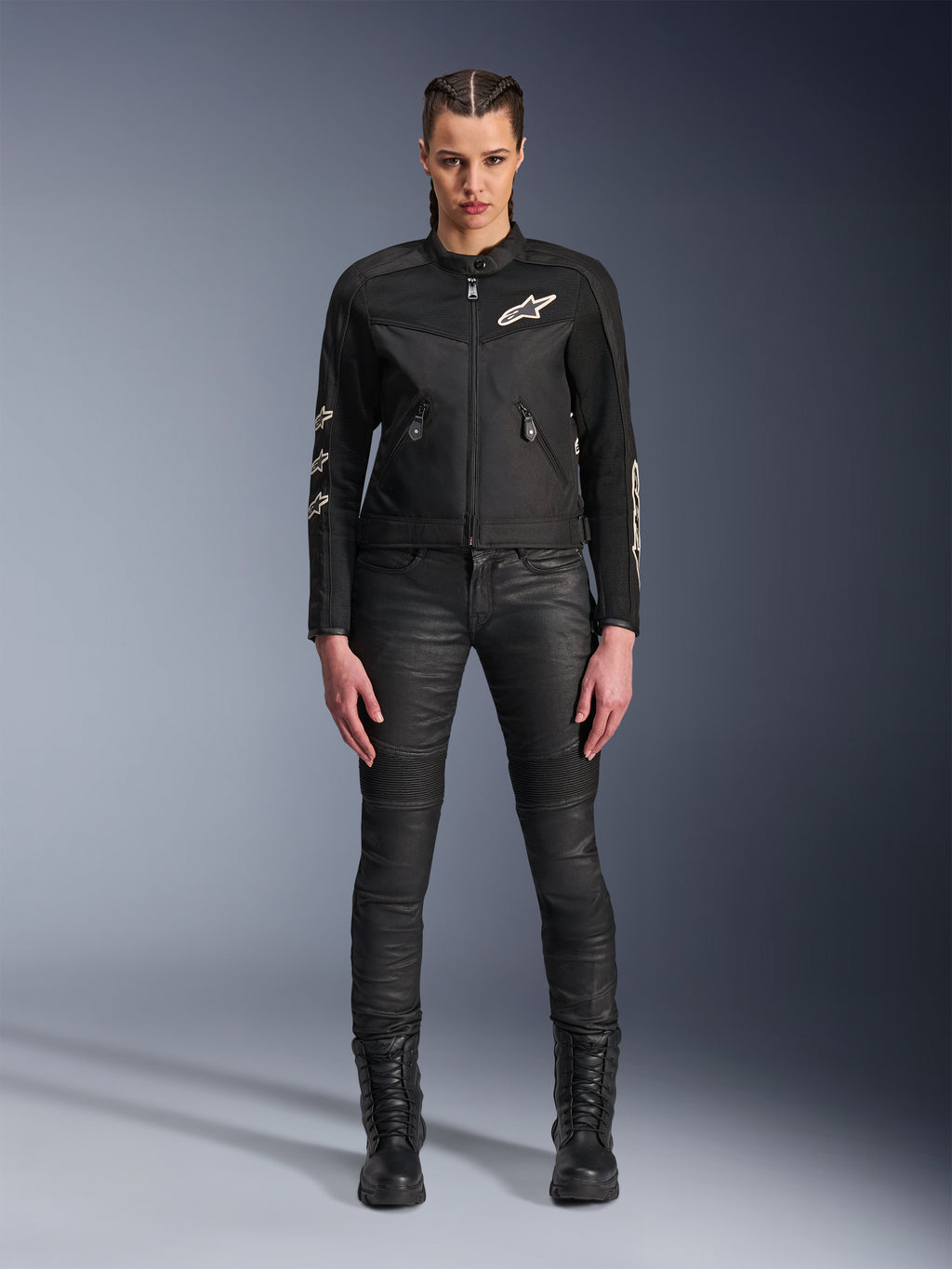 Vrouwelijk model draagt de Alpinestars Stella T-Dyno Air Jas, zwarte motorjas voor dames, voorzien van 3D-meshpanelen en witte Astars-logo's, gecombineerd met een zwarte slim-fit motorbroek en zwarte veterlaarzen, urban motorkledingstijl.