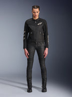 Vrouwelijk model draagt de Alpinestars Stella T-Dyno Air Jas, zwarte motorjas voor dames, voorzien van 3D-meshpanelen en witte Astars-logo's, gecombineerd met een zwarte slim-fit motorbroek en zwarte veterlaarzen, urban motorkledingstijl.