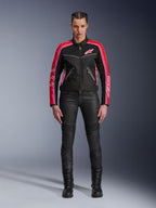 Motorradfahrerin in der Alpinestars Stella T-Dyno Air Jacke, Schwarz mit hellroten und fuchsiafarbenen Akzenten, kombiniert mit schwarzer Motorradhose und Schnürstiefeln, mit 3D-Mesh-Einsätzen, taillierter Passform und pinkfarbenen Stern-Logos, urbanes Motorrad-Outfit