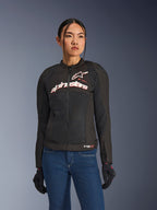 Femme portant la veste Alpinestars Stella SMX Air, noir, blanc et rouge fluo, veste de moto en textile avec maille ventilée et logo blanc sur la poitrine, associée à un jean bleu et des gants de moto noirs, coupe féminine pour la conduite sportive