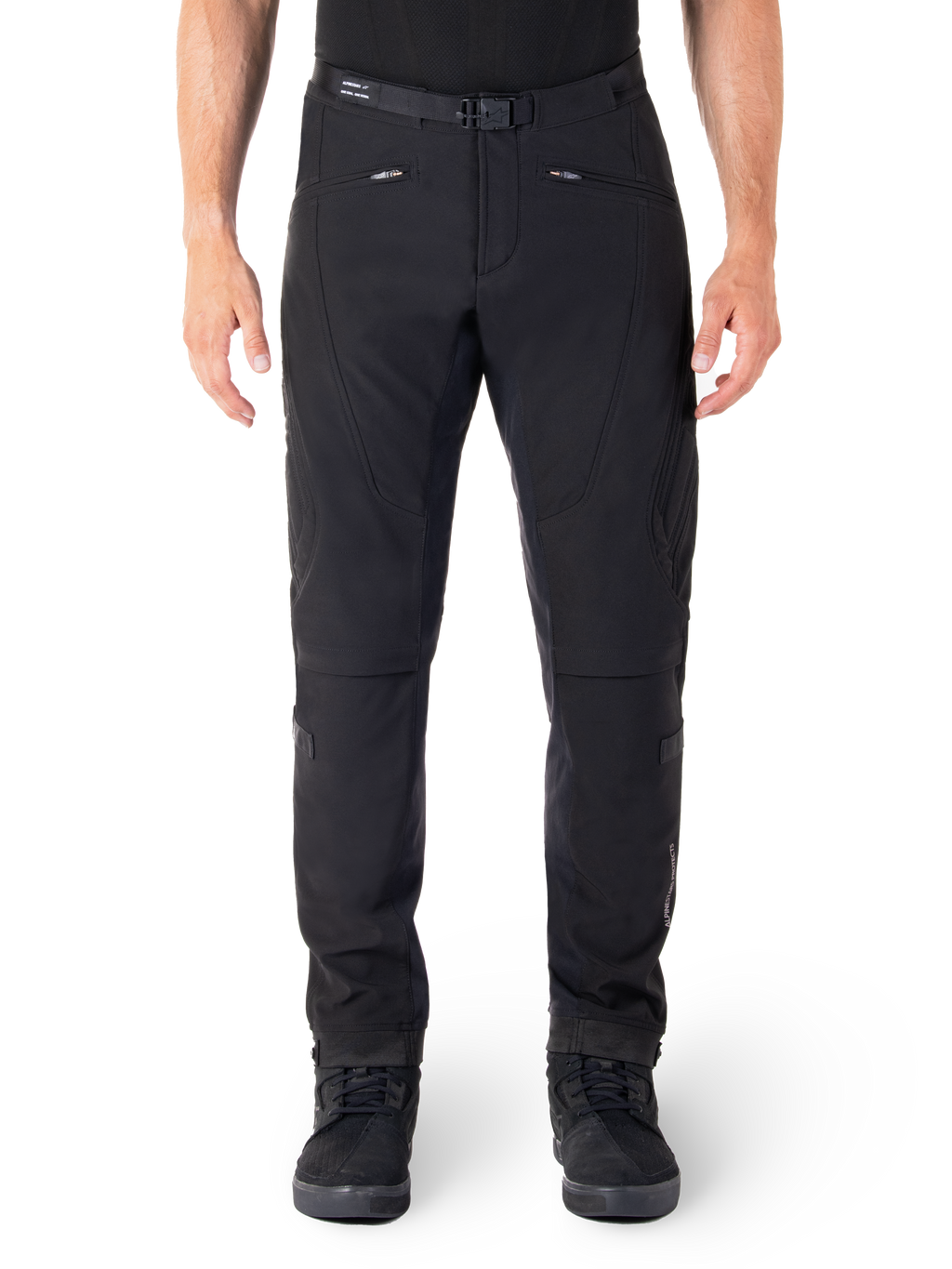 Pantalon Alpinestars Alden, pantalon de moto urbain noir, vue de face, tissu softshell technique extensible, ceinture intégrée avec boucle magnétique, poches avant zippées, détails matelassés aux genoux, silhouette ajustée, porté avec des chaussures de moto noires