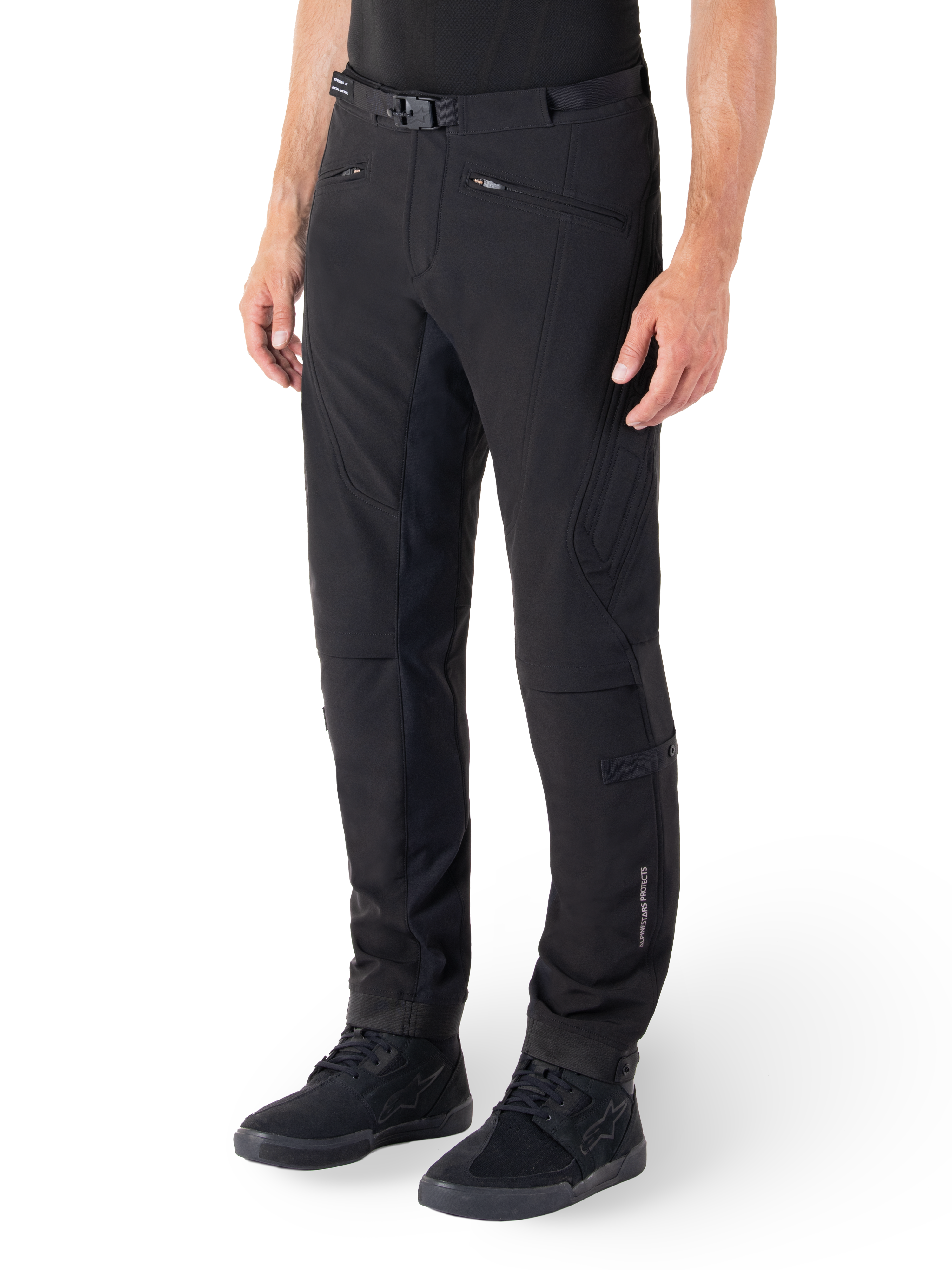 Pantalon Alpinestars Alden, pantalon de moto urbain, noir, tissu softshell technique avec coupe régulière, doté d'une boucle de taille magnétique, d'empiècements latéraux matelassés, de poches zippées et d'un logo discret sur le bas de la jambe, porté avec des chaussures de moto noires