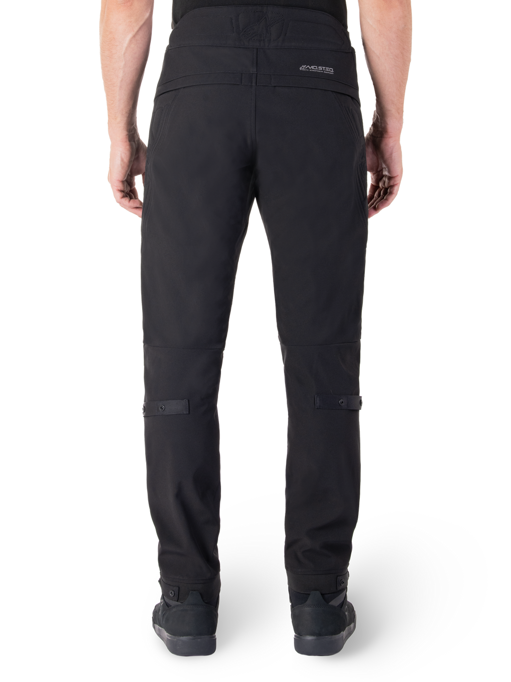 Pantalon Alpinestars Alden, pantalon de moto urbain noir, vue arrière, avec mot-symbole réfléchissant MO.ST.EQ. sur l'empiècement arrière, coupe ajustée sous le genou et boutons-pression de réglage du volume aux mollets et aux chevilles, design textile technique d'inspiration streetwear.