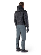 Alpinestars Alden broek, urban motorbroek, Urban Gray, achteraanzicht van een motorrijder die een zwart gewatteerd jack met capuchon en motorsneakers draagt, voorzien van een slanke pasvorm onder de knie met zwarte stretchpanelen en knieverstellers, modern op streetwear geïnspireerd ontwerp.