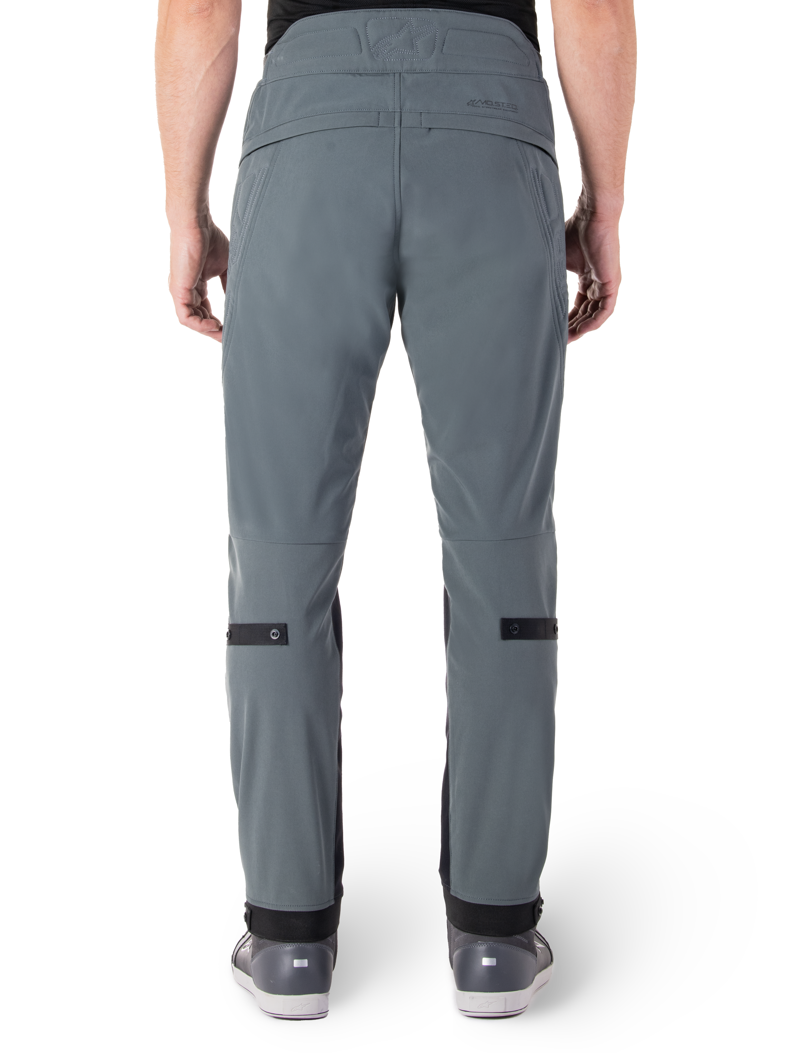 Alpinestars Alden broek, Urban Gray, achteraanzicht van een stedelijke motorbroek voor heren, slim fit onder de knie met zwarte verstelbanden op de kuiten, ontwerp met hoge taille voorzien van het MO.ST.EQ.-woordmerk op de achterpas, gedragen met grijze rijdschoenen