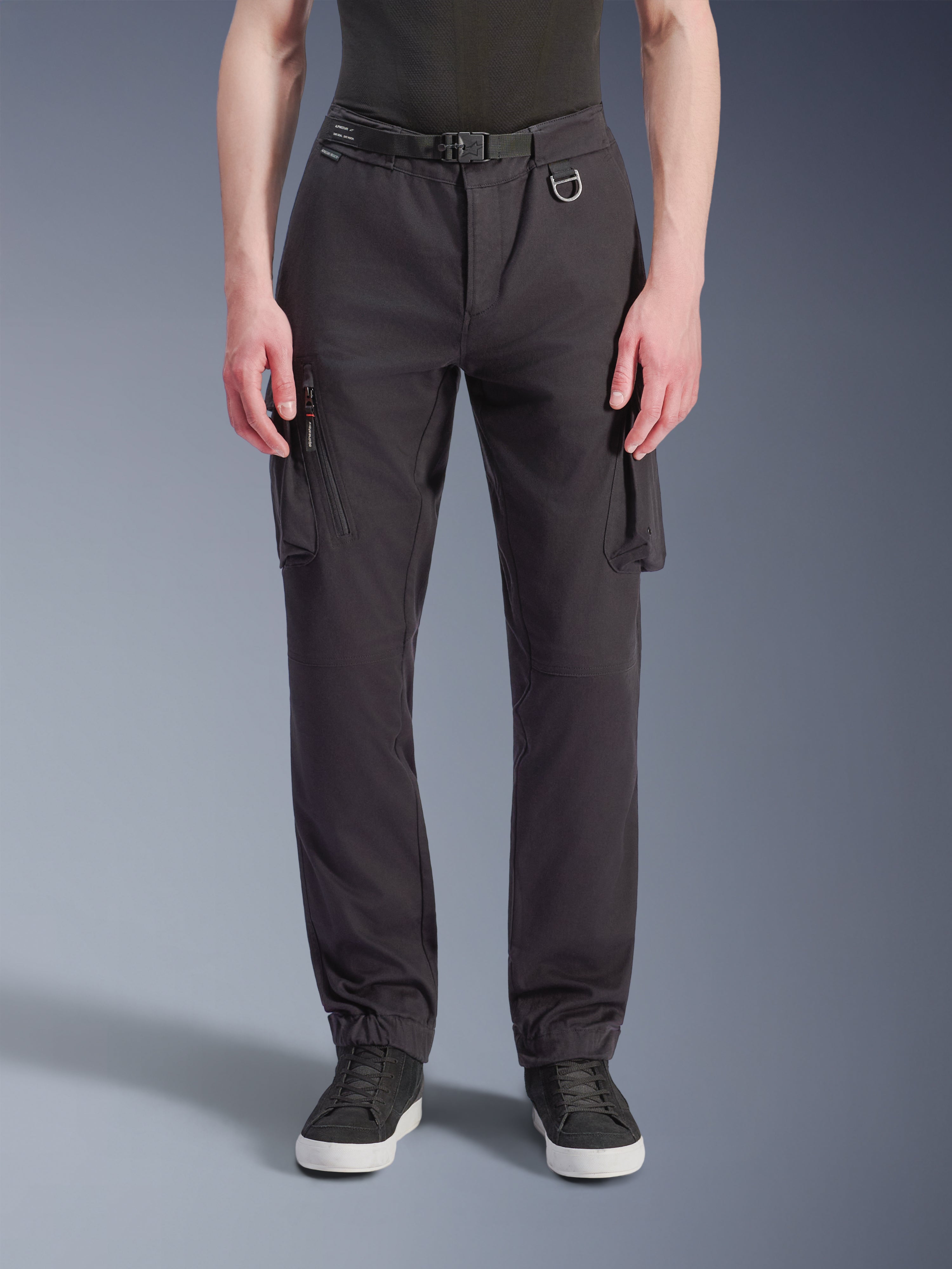 Alpinestars Flex-AST Cargo Pants - Short, zwarte stedelijke motorbroek, vooraanzicht met technische stretchstof, meerdere cargozakken met ritsdetails aan de zijkanten, metalen D-ring riemlus, regular tapered pasvorm met elastische zomen, gedragen met zwarte sneakers