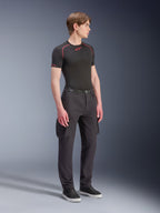 Mannelijk model draagt Alpinestars Flex-AST Cargo Pants - Short in het zwart, urban motorcargobroek met zijzakken en taps toelopende pijpen, gestyled met een zwarte base layer en sneakers, stedelijke motorkleding.