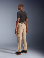 Alpinestars Flex-AST Cargo Pants, stedelijke motorbroek, lichtbeige, gedragen door een model vanuit een zij-achteraanzicht, voorzien van functionele cargozakken en elastische boorden, gestyled met een zwart shirt met korte mouwen en zwarte sneakers.