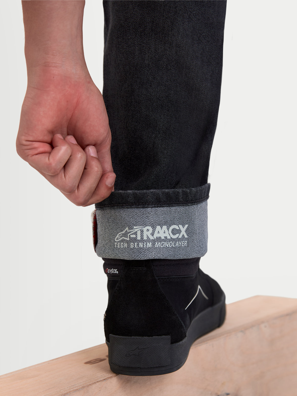 Alpinestars Flex-AST 8 Denim Pants Short, pantalon moto urbain noir, vue détaillée montrant le revers retroussé avec le marquage A-TRAACX tech denim monolayer et des chaussures