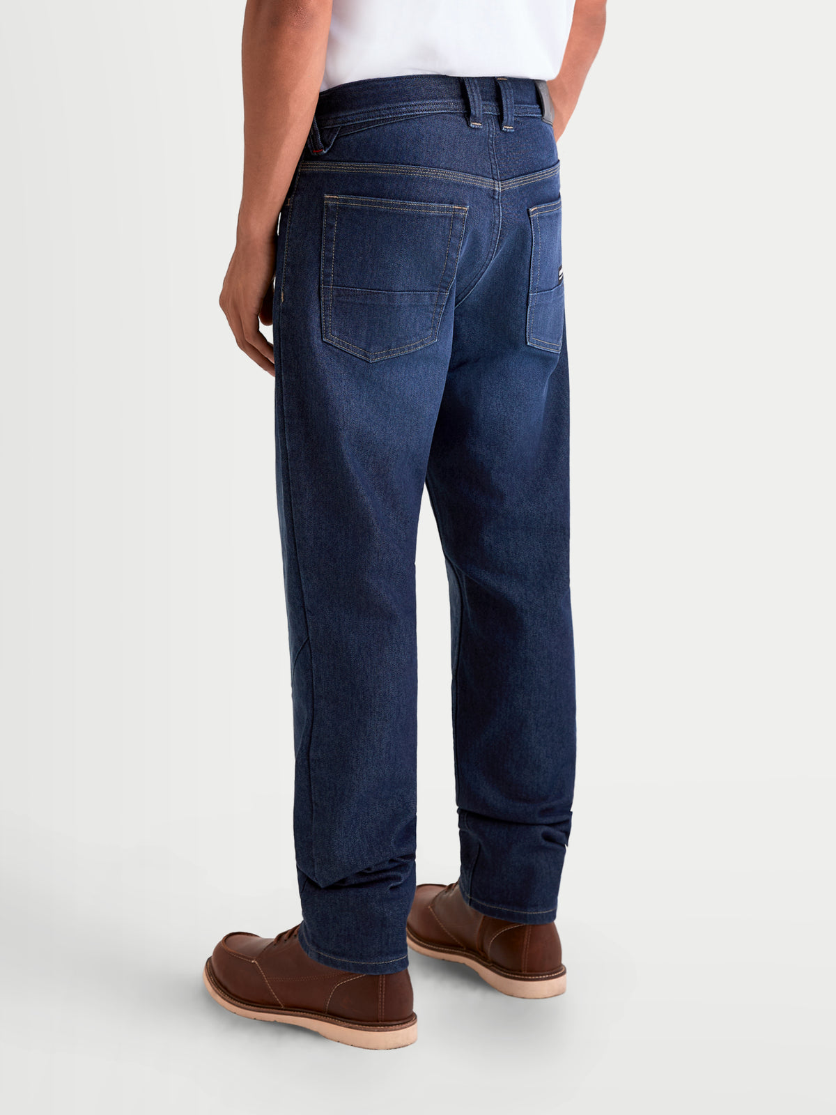 Alpinestars Flex Ast 7 Denim Broek Short, urbane motorjeans voor heren in donkerblauw, achteraanzicht op model met casual motoruitrusting en bruine leren laarzen, met enkellaagse technische denim constructie en vijf-zakkenstijl