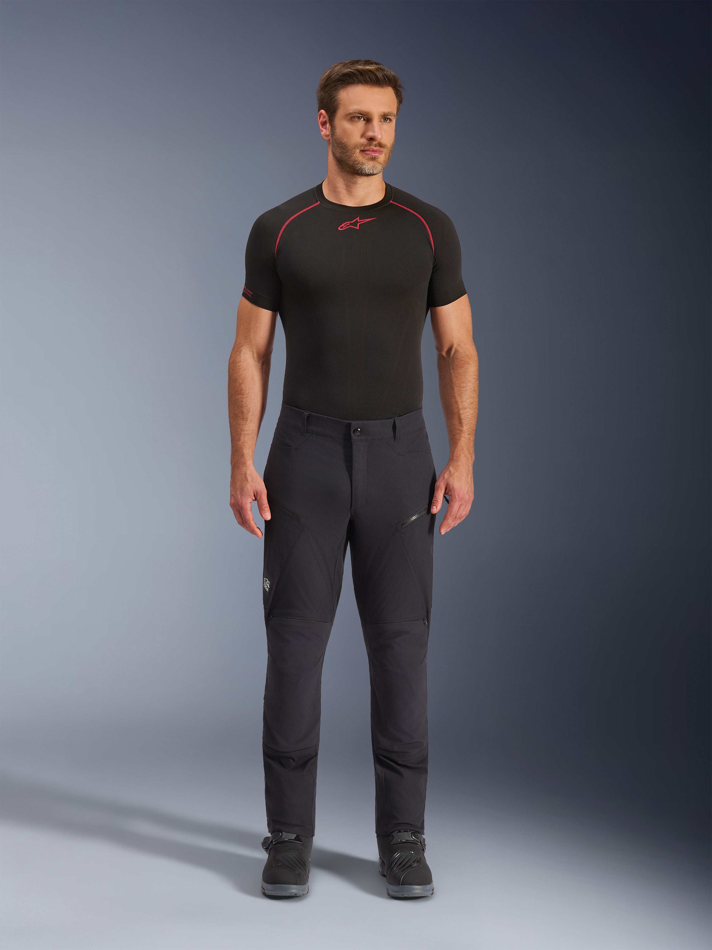 Alpinestars Flex-AST Explorer Pants, Black adventure touring motorcycle pants, man wearing fitted textile riding pants with zippered cargo pockets and reinforced panels, styled with a black base layer and motorcycle boots, durable protection for adventure riding