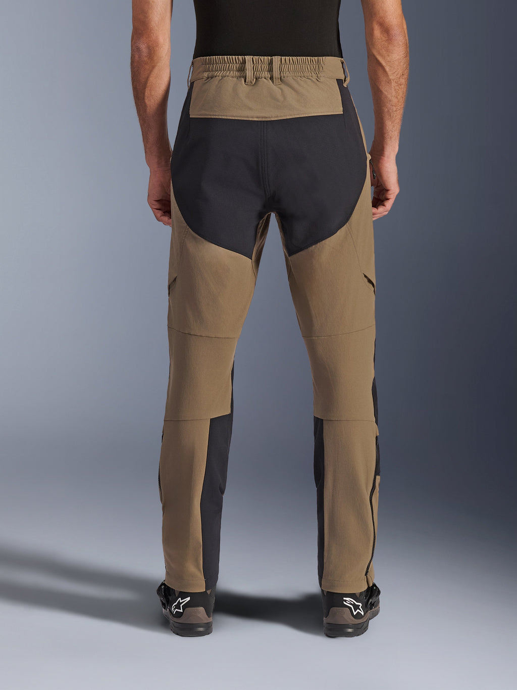 Alpinestars Flex-AST Explorer Hose, Adventure-Motorradhose, Walnut Black, Rückansicht am Fahrer getragen, schwarze Ripstop-Verstärkungspanels am Gesäß und an den Beininnenseiten, elastischer Bund, lange Reißverschlüsse an den Unterschenkeln und passende Adventure-Stiefel
