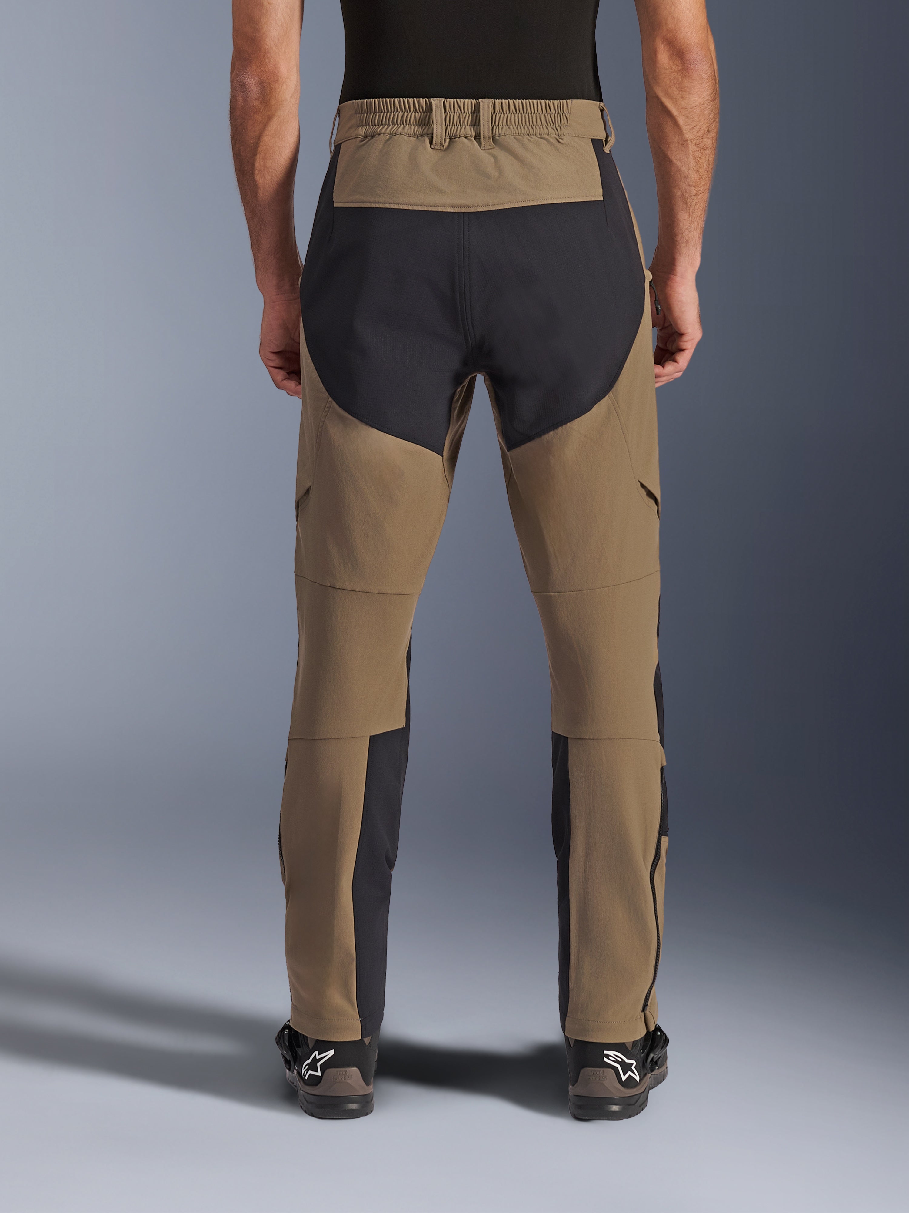 Alpinestars Flex-AST Explorer Hose, Adventure-Motorradhose, Walnut Black, Rückansicht am Fahrer getragen, schwarze Ripstop-Verstärkungspanels am Gesäß und an den Beininnenseiten, elastischer Bund, lange Reißverschlüsse an den Unterschenkeln und passende Adventure-Stiefel