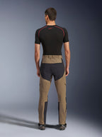Alpinestars Flex-AST Explorer Hose, Walnut Black, Rückansicht am Modell, mit verstärktem schwarzem Gesäßbereich und braunem Stretch-Textil, kombiniert mit schwarzem Baselayer und technischen Motorradstiefeln, strapazierfähige Adventure-Motorradbekleidung