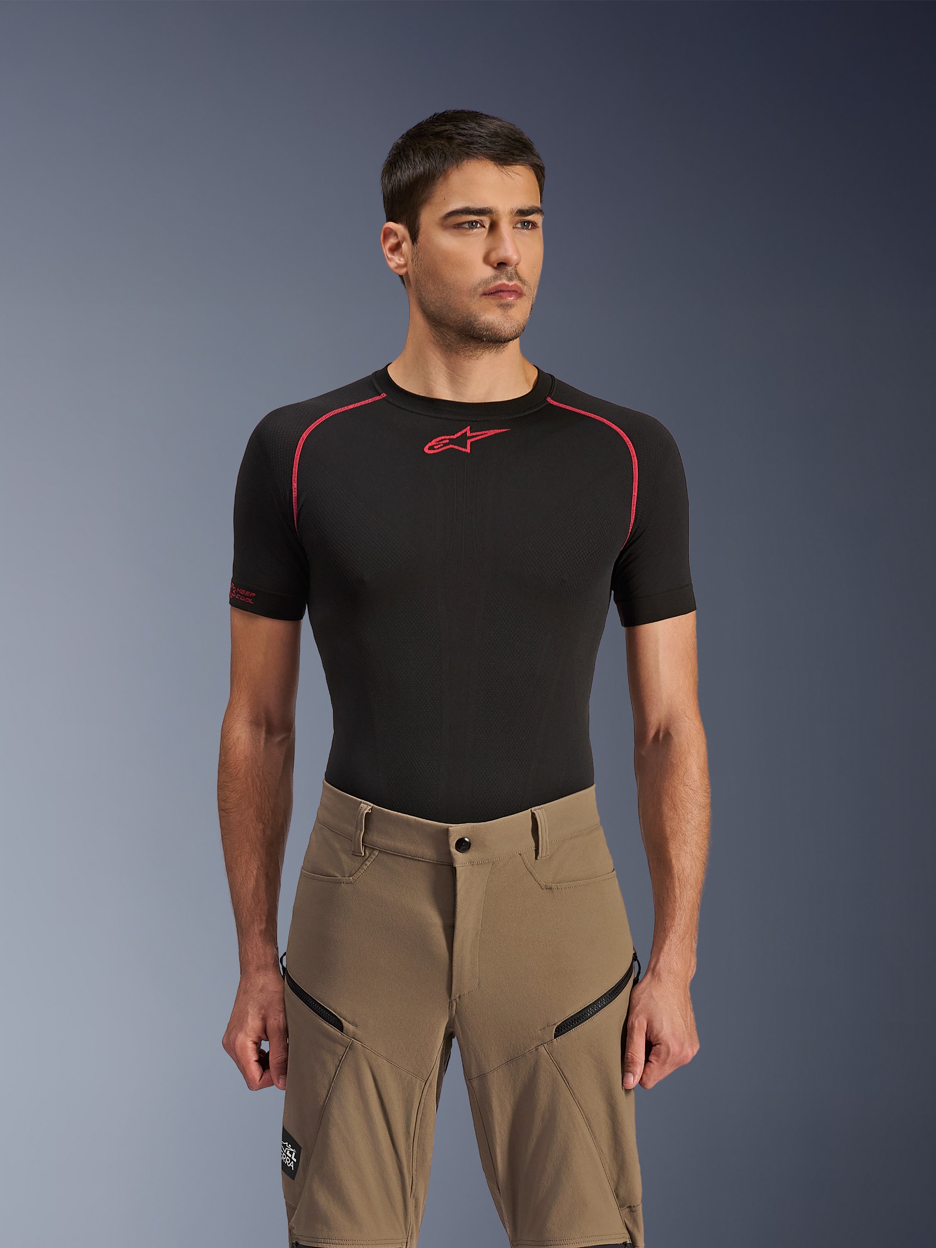 Alpinestars Flex-AST Explorer Hose, Adventure-Motorradhose, Walnut Black, getragen von einem Modell mit schwarzem Base-Layer-Shirt, mit diagonalen Reißverschluss-Cargotaschen und strapazierfähiger Stretch-Textilkonstruktion.